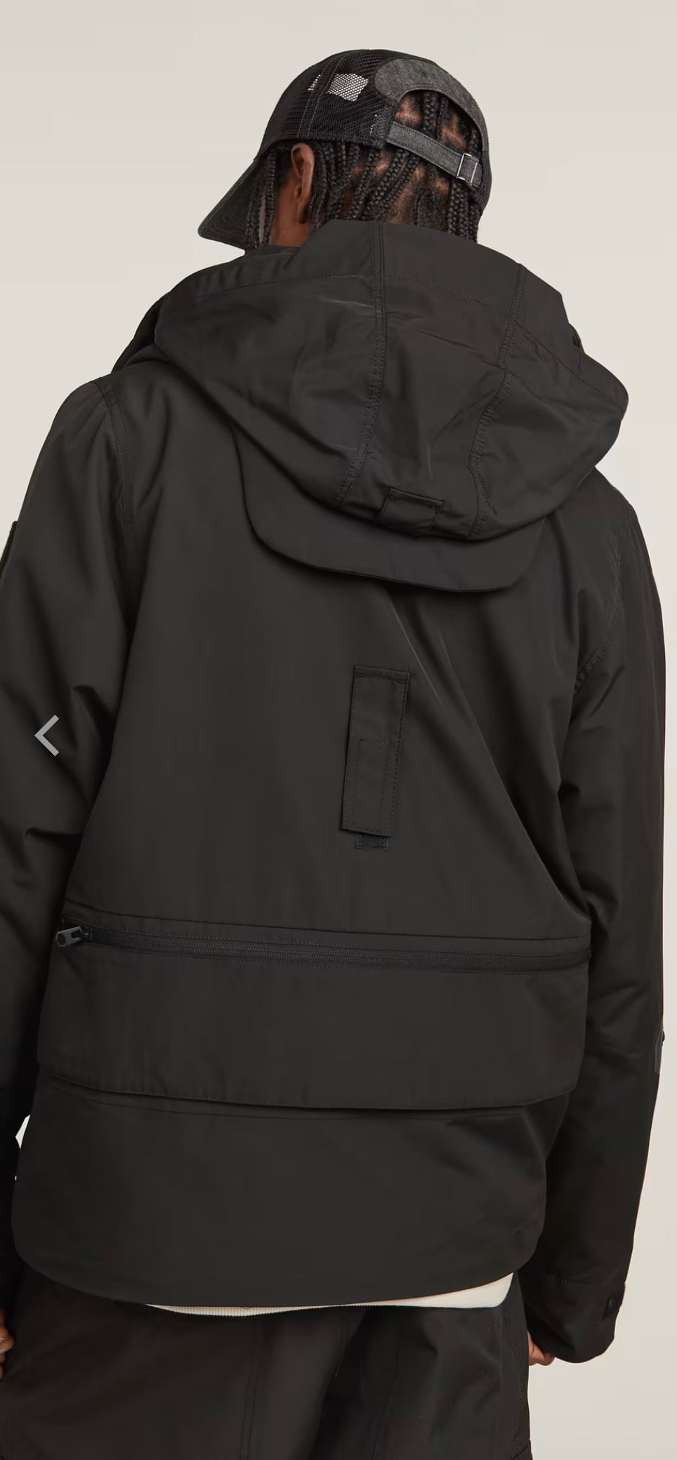 Person wearing a black hooded jacket on a light gray background