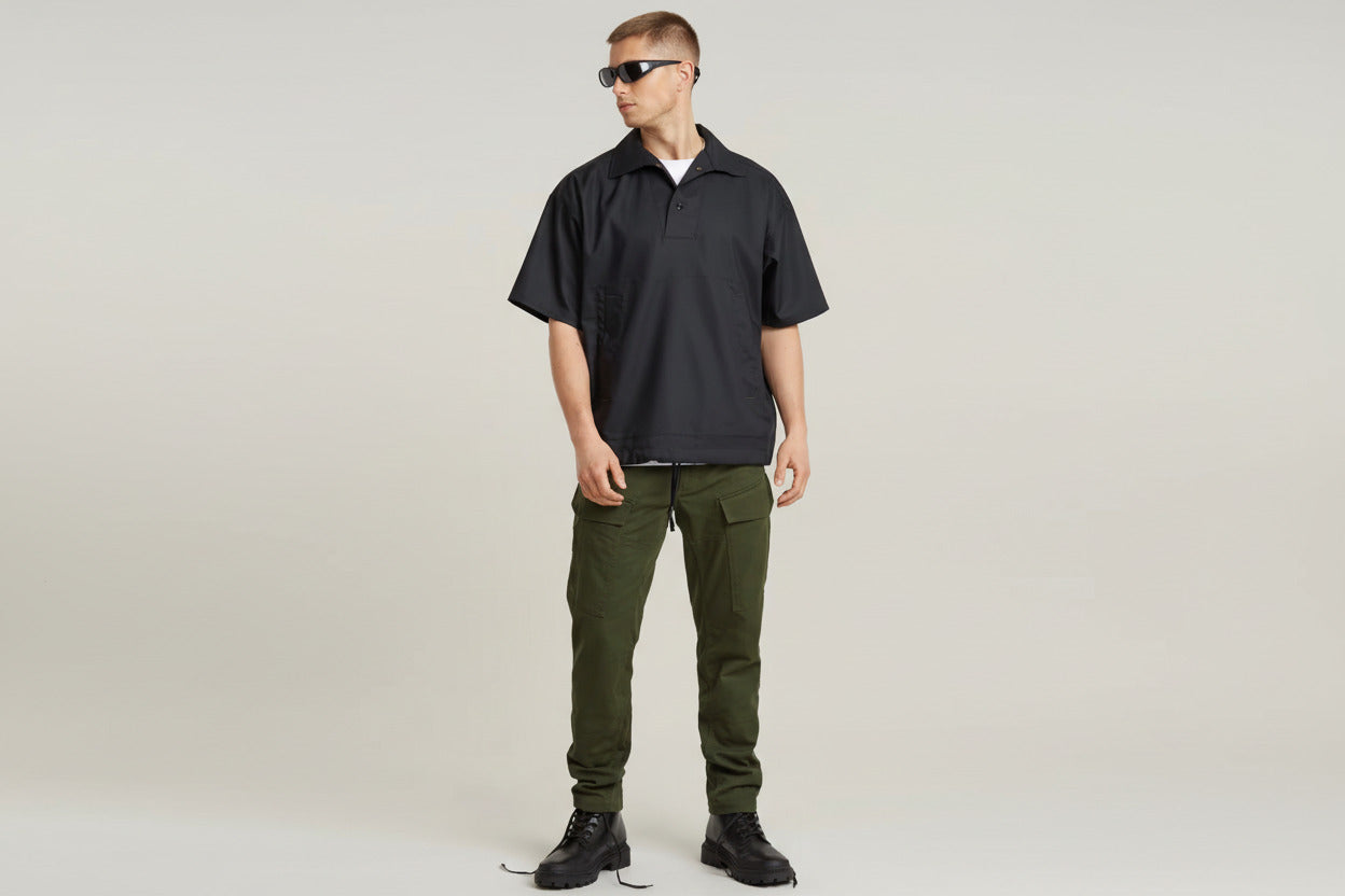 Person wearing a black short-sleeve shirt and green pants on a plain background