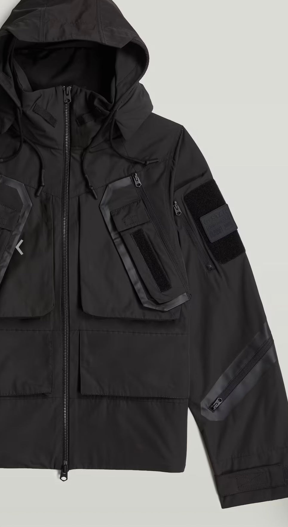 Black tactical jacket with multiple pockets and patches on a light gray background