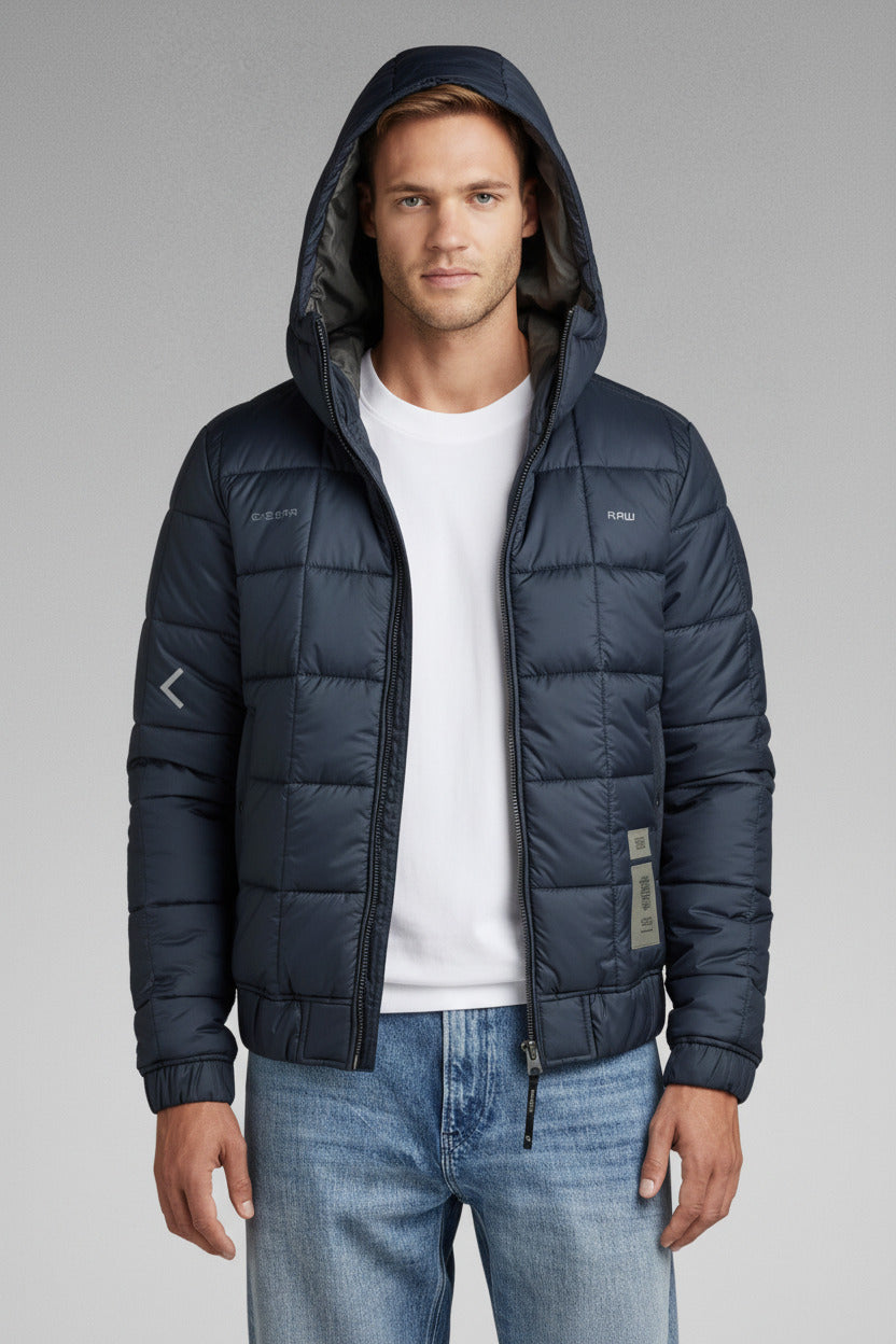 Man wearing a navy puffer jacket with a hood on a gray background