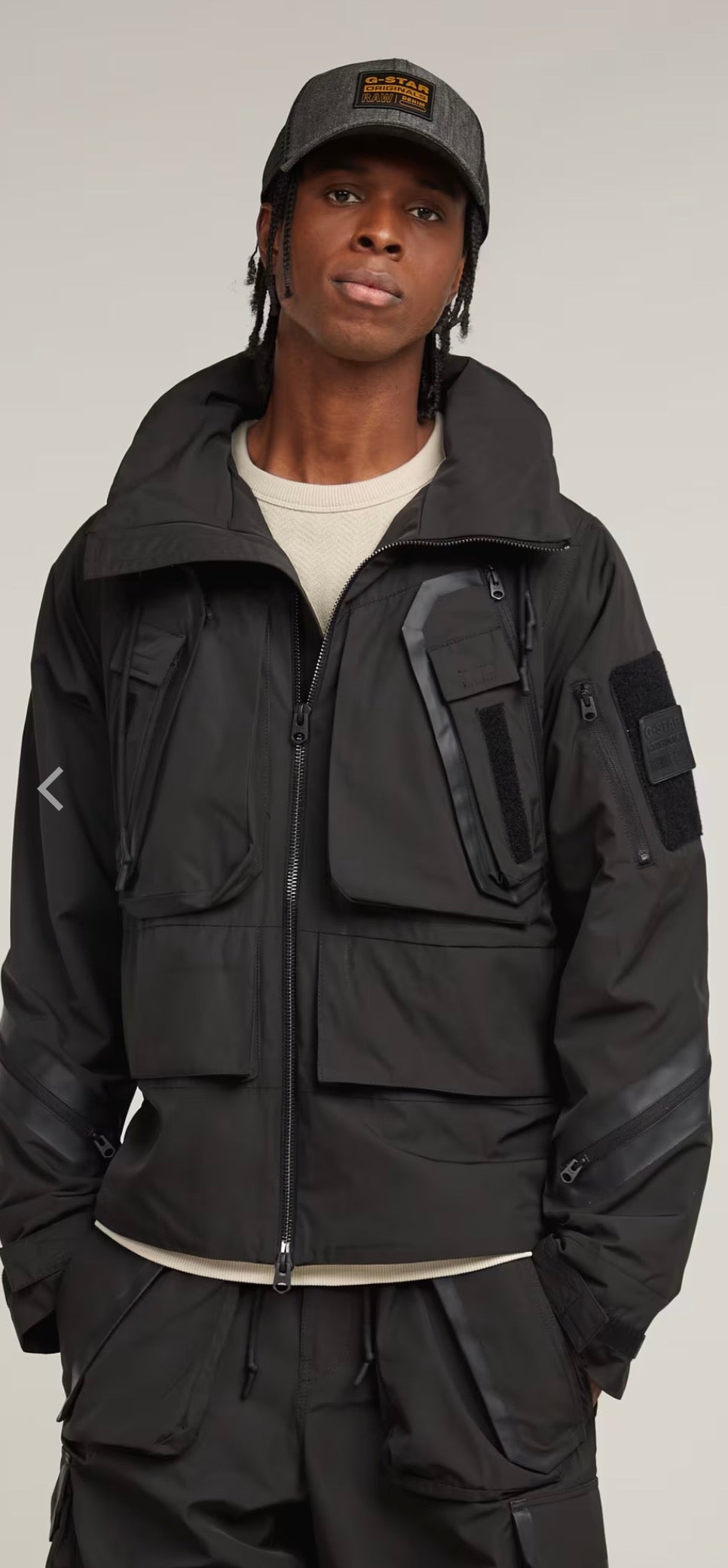 Person wearing a black tactical jacket and cap on a gray background