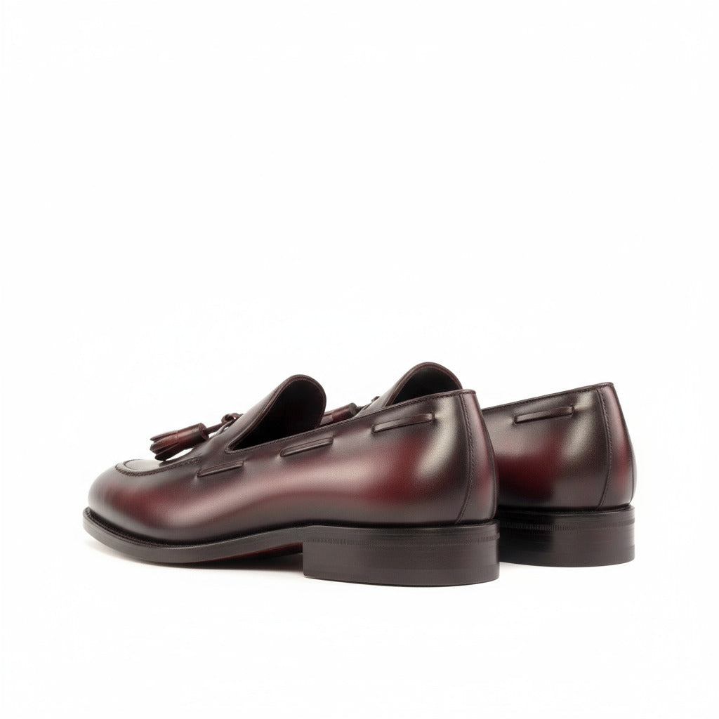 Pair of maroon loafers with tassels on a white background
